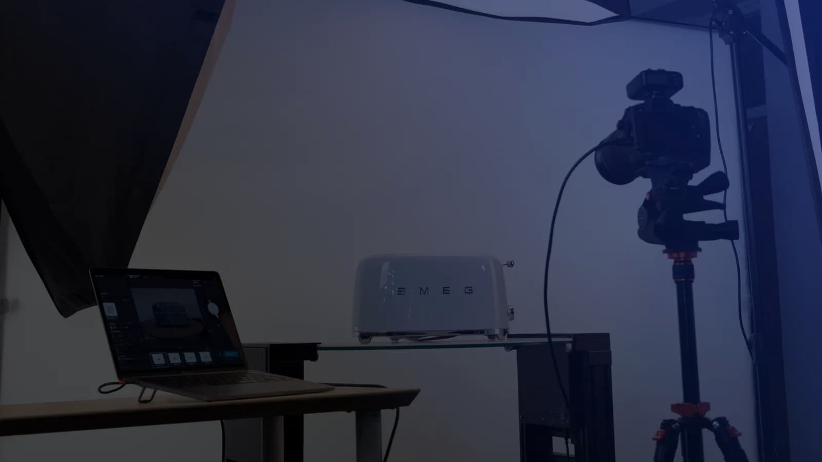 Produktfotostudio med tethering - en laptop med opptaksprogramvare ved siden av et kamera på stativ og et produkt på en glasshylle